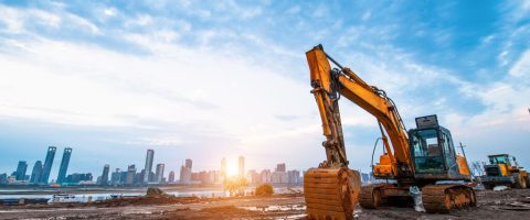 Excavator in construction site on sunset sky background. Development, heavy machinery.